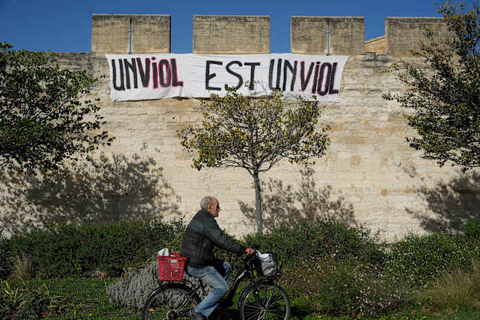 BESTAND - Een man fietst voor een spandoek met de tekst: "Een verkrachting is een verkrachting," in Avignon, Zuid-Frankrijk, op 16 oktober 2024. (AP Photo/Lewis Joly, Bestand)