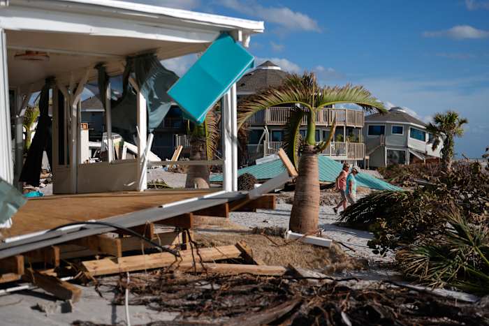 BESTAND - Inwoner Kerry Flynn, rechts, en een vriend lopen langs een beschadigd huis en het verplaatste dak van de tiki-hut van hun 55+ stacaravangemeenschap na de passage van orkaan Milton, op Manasota Key, in Englewood, Florida, 13 oktober 2024. (AP-foto/Rebecca Blackwell, bestand)