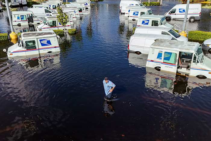 Een USPS-medewerker inspecteert vrachtwagens die waren verplaatst om ze tegen de wind te beschermen, maar die nu onder water staan, omdat intense regen van de orkaan Milton ervoor zorgde dat de Anclote River op vrijdag 11 oktober 2024 overstroomde in New Port Richey, Florida. (AP Photo / Mike Carlson)