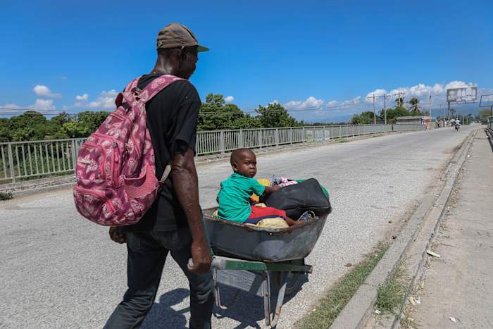 Een man duwt een kind in een kruiwagen door een straat in Pont-Sonde, Haïti, maandag 7 oktober 2024, dagen nadat een bende de stad had aangevallen. (AP-foto/Odelyn Joseph)