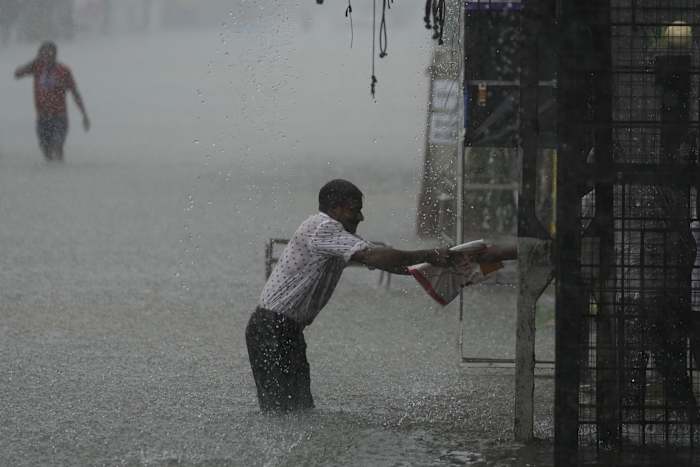 Een man zoekt een veilige plek terwijl het regent in een ondergelopen straat in Colombo, Sri Lanka, zondag 13 oktober 2024. (AP Photo/Eranga Jayawardena)