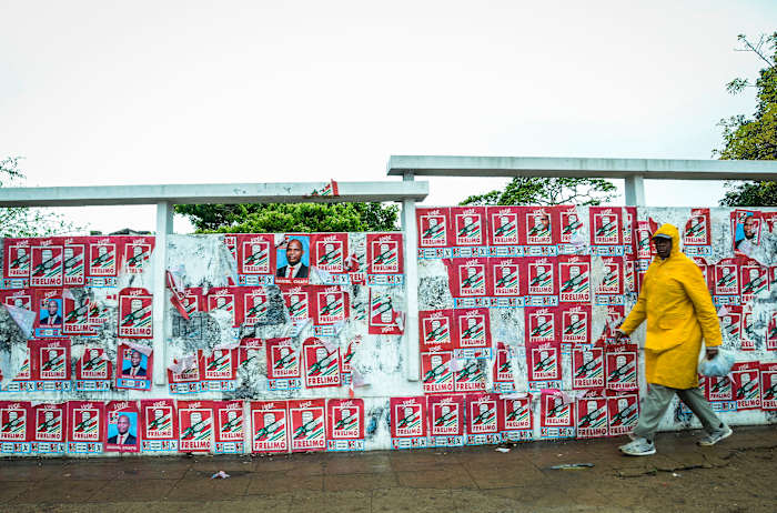 Een voetganger passeert een muur met verkiezingsposters in Maputo, zondag 6 oktober 2024, voorafgaand aan de verkiezingen in Mozambique. (AP Foto/Carlos Uqueio)