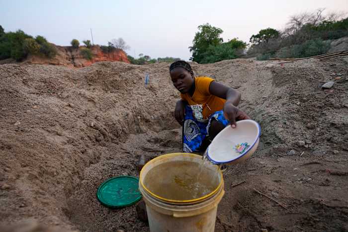 Een vrouw schept water uit een gat dat ze heeft gegraven in een opgedroogde rivierbedding in Lusitu, Zambia, woensdag 18 september 2024. (AP Photo/Themba Hadebe)