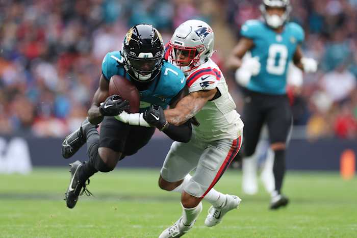 Jacksonville Jaguars wide receiver Brian Thomas Jr. (7) wordt aangepakt door New England Patriots cornerback Christian Gonzalez (0) tijdens de eerste helft van een NFL-voetbalwedstrijd, zondag 20 oktober 2024, in Londen. (AP-foto/Ian Walton)