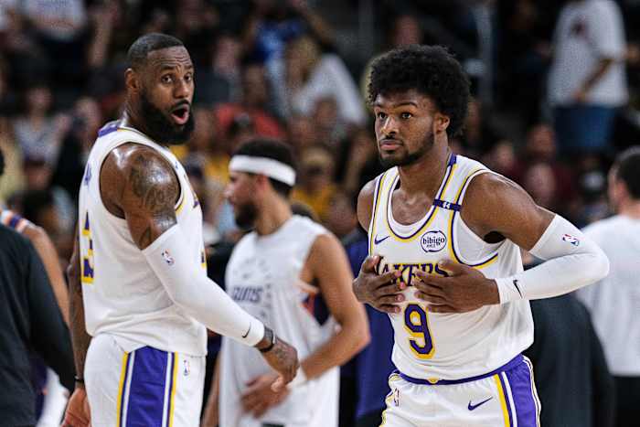Los Angeles Lakers-bewaker Bronny James (9), rechts, stapt het veld op met Los Angeles Lakers-aanvaller LeBron James (23) tijdens de eerste helft van een NBA-basketbalwedstrijd voor het seizoen op zondag 6 oktober 2024 in Palm Desert, Californië. (AP-foto/William Liang)