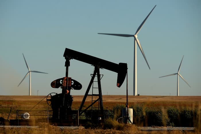 Op de voorgrond werkt een jaknikker terwijl windturbines van het Buckeye Wind Energy-windpark in de verte werken, maandag 30 september 2024, nabij Hays, Kan. (AP Photo/Charlie Riedel)