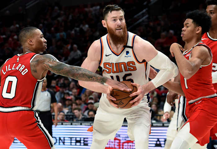 Phoenix Suns-centrum Aron Baynes, midden, rijdt naar de basket tussen Portland Trail Blazers-bewakers Damian Lillard, links, en Anfernee Simons, rechts, tijdens de tweede helft van een NBA-basketbalwedstrijd in Portland, Oregon, dinsdag 10 maart 2020. De Blazers wonnen met 121-105. (AP-foto/Steve Dykes)