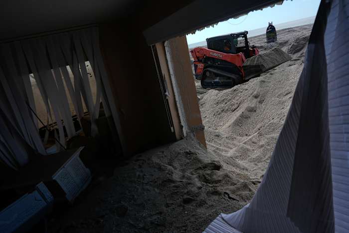 Scott Bennett, een aannemer die gespecialiseerd is in stormherstel, verwijdert zand van ongeveer 1,5 meter diep van de patio van een condominium aan het strand in Venetië, Florida, na de passage van de orkaan Milton, zaterdag 12 oktober 2024. (AP Photo/Rebecca Blackwell)