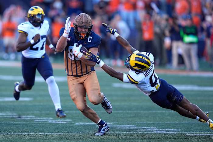 Tanner Arkin uit Illinois ontwijkt een tackle van Semaj Morgan uit Michigan op een nep-punter tijdens de tweede helft van een NCAA-universiteitsvoetbalwedstrijd op zaterdag 19 oktober 2024 in Champaign, Illinois. (AP Photo/Charles Rex Arbogast)