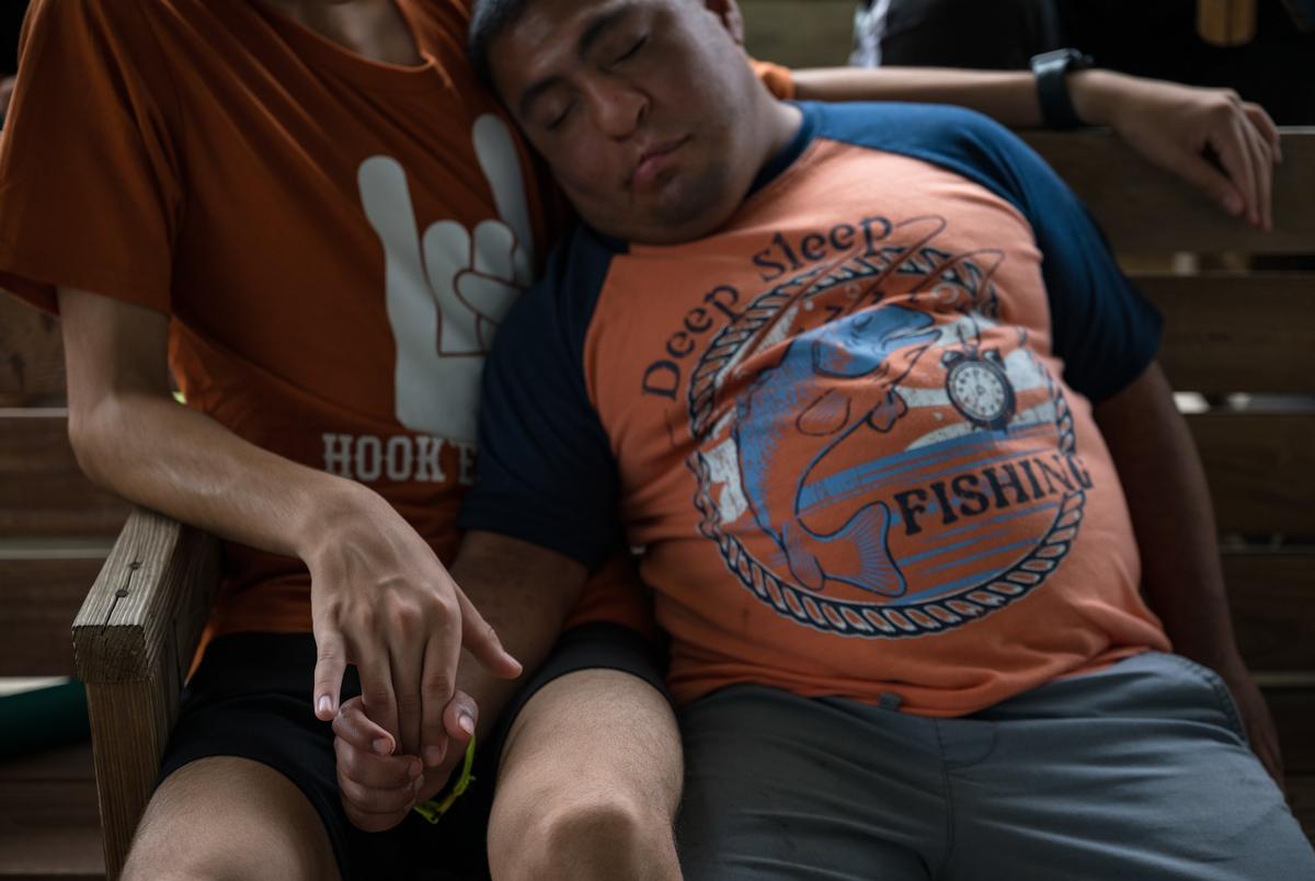 Mario, een camper in Camp Camp, recht, houdt handen vast met zijn counselor, augustus, terwijl hij een dutje doet tijdens Target Sports Hour op dinsdag 22 juli 2025, in Center Point. Camp Camp is een zomerkamp georganiseerd door Children's Association voor maximaal potentieel voor mensen met een handicap en heropend kort na de overstromingen van 4 juli om een normale zomerervaring voor hun kampeerders te bieden. Sommige voogden, zoals die van Mario, kozen ervoor om hun familieleden niet naar het kamp te sturen onmiddellijk na de overstroming, maar stuurden ze in plaats daarvan na het normaliseren van de ramp.